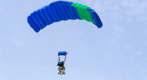 Tandem Skydiving pair gliding beneath a colorful parachute against a bright blue sky with white clouds during the peaceful descent after freefall.