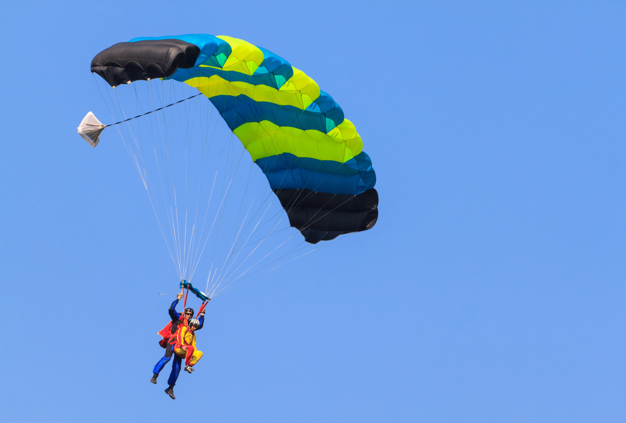 A thrilling tandem skydiving experience captured from below against a cloudless blue sky.