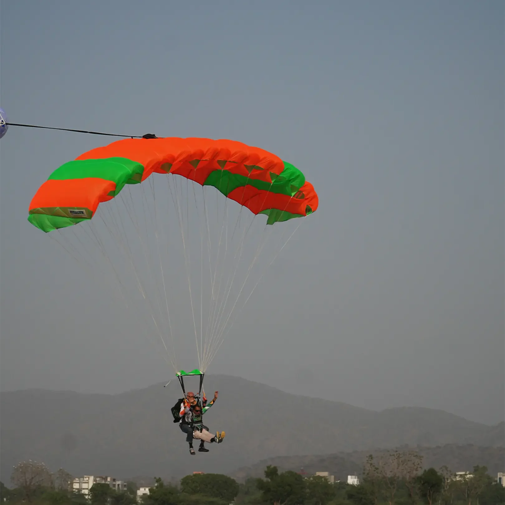 Skydiver under an orange canopy approaching the landing area near Mount Abu, Rajasthan